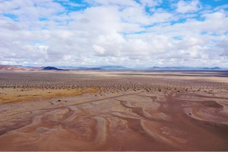 Aerial photograph of the desert near Beatty, Nevada, with winding sand patterns under a cloudy sky. Photo by JD Garrett.