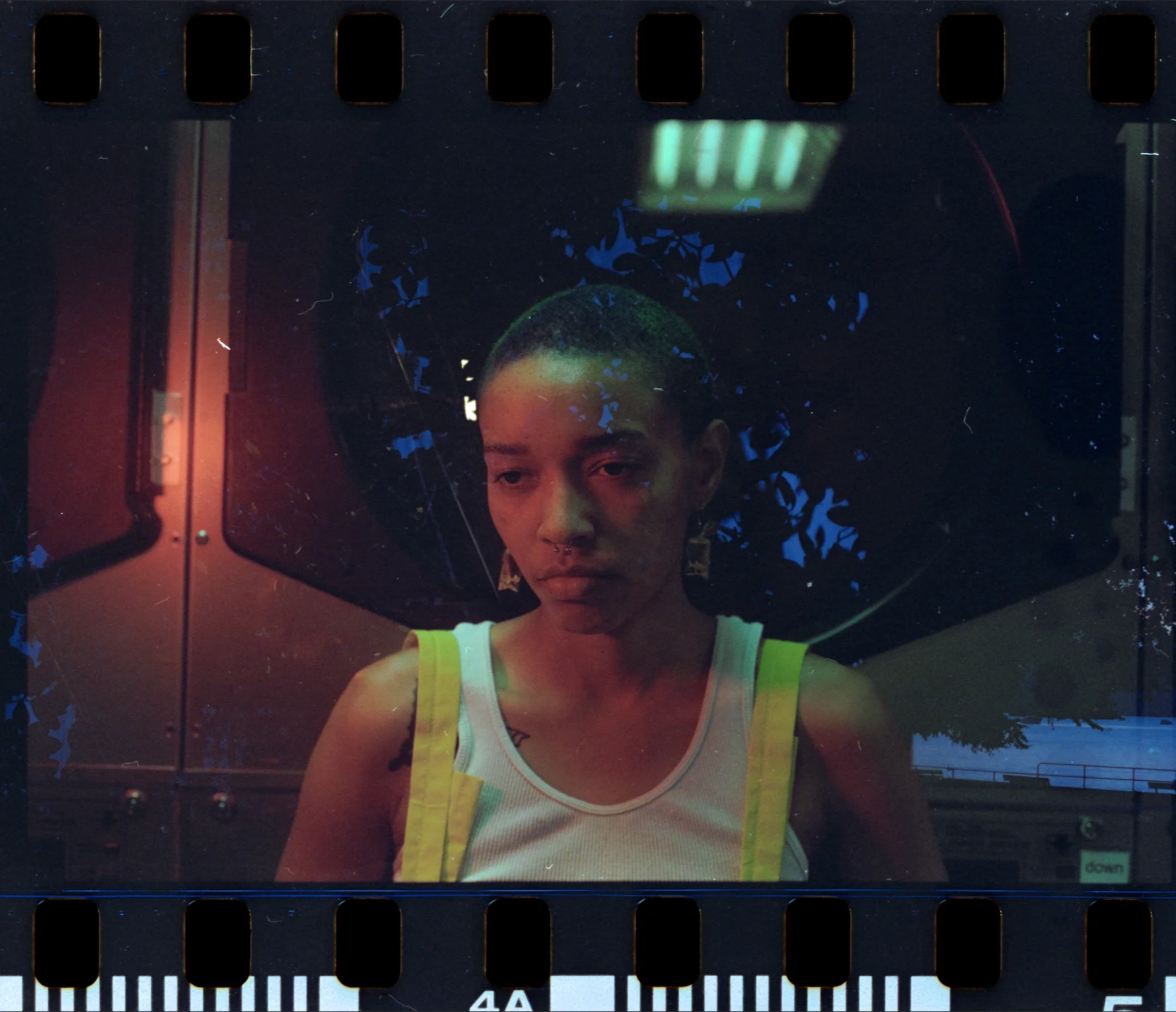 Portrait of a person in a white tank top under moody red and blue light, framed by film sprockets and texture, from the series Long Gone by Merima Agovic.
