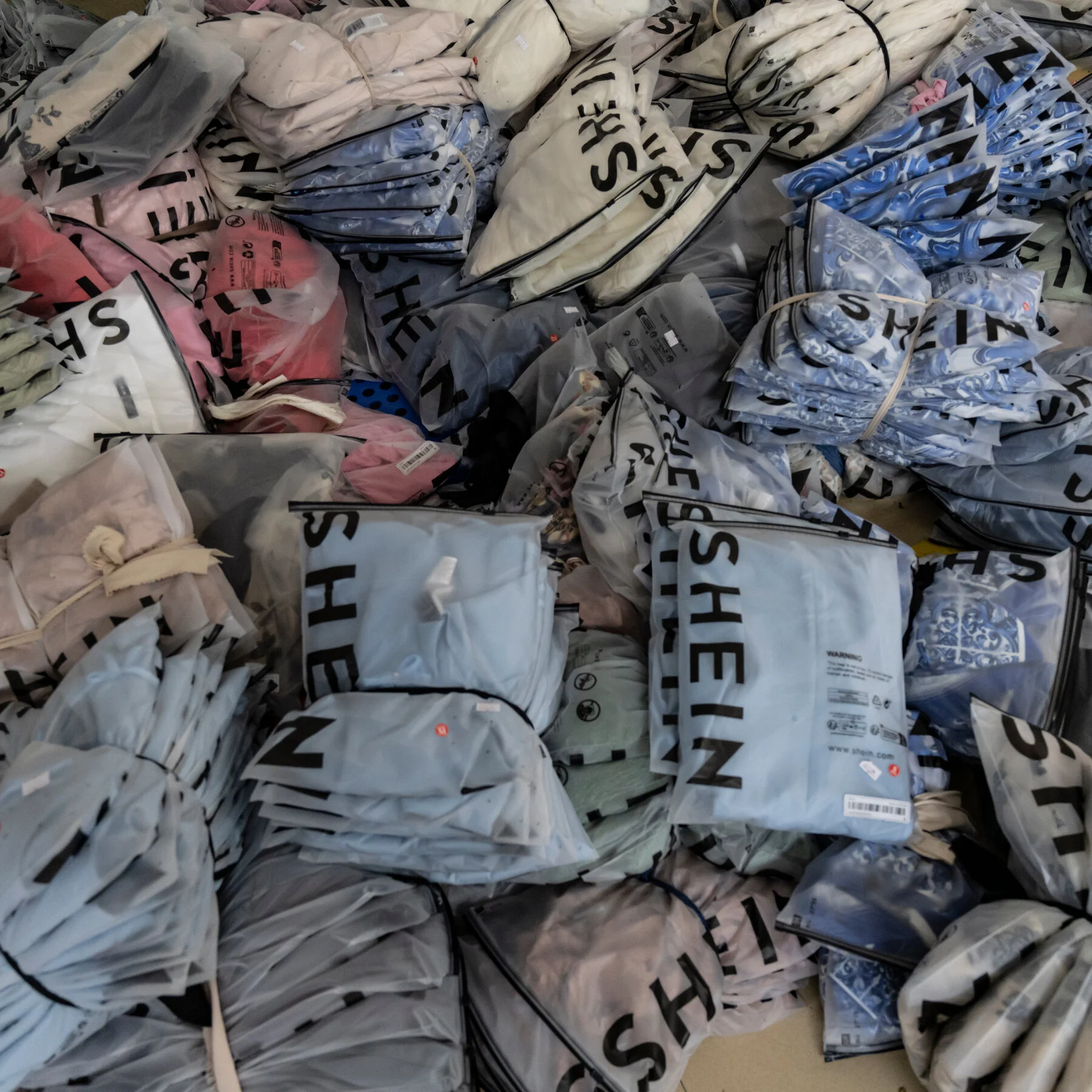 Piles of individually wrapped Shein clothing items in plastic bags, showing mass-produced fast fashion ready for shipment.