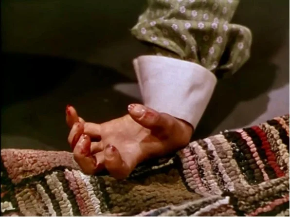 Close-up of a bloodied hand lying on a striped rug in a scene from the Western film Rancho Notorious (1952), directed by Fritz Lang.