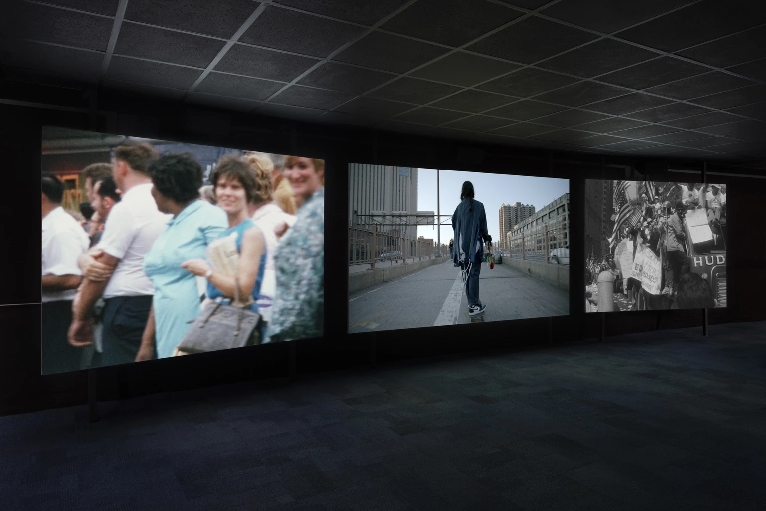Three-channel video installation by Naeem Mohaiemen at Artangel, showing crowds, a lone skateboarder in a city, and a protest scene projected in a dark gallery.