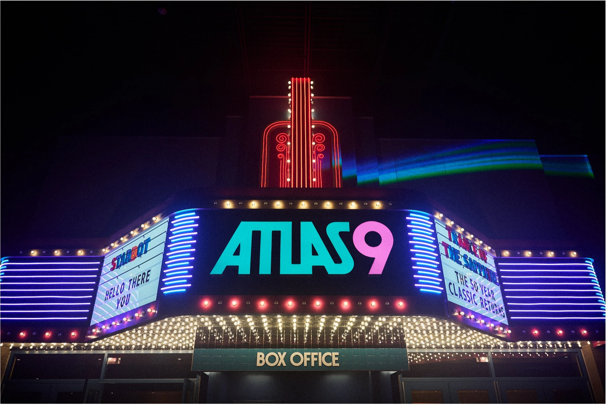 Neon-lit Atlas 9 cinema marquee and box office at night, with colorful lights and signage glowing against a dark sky.