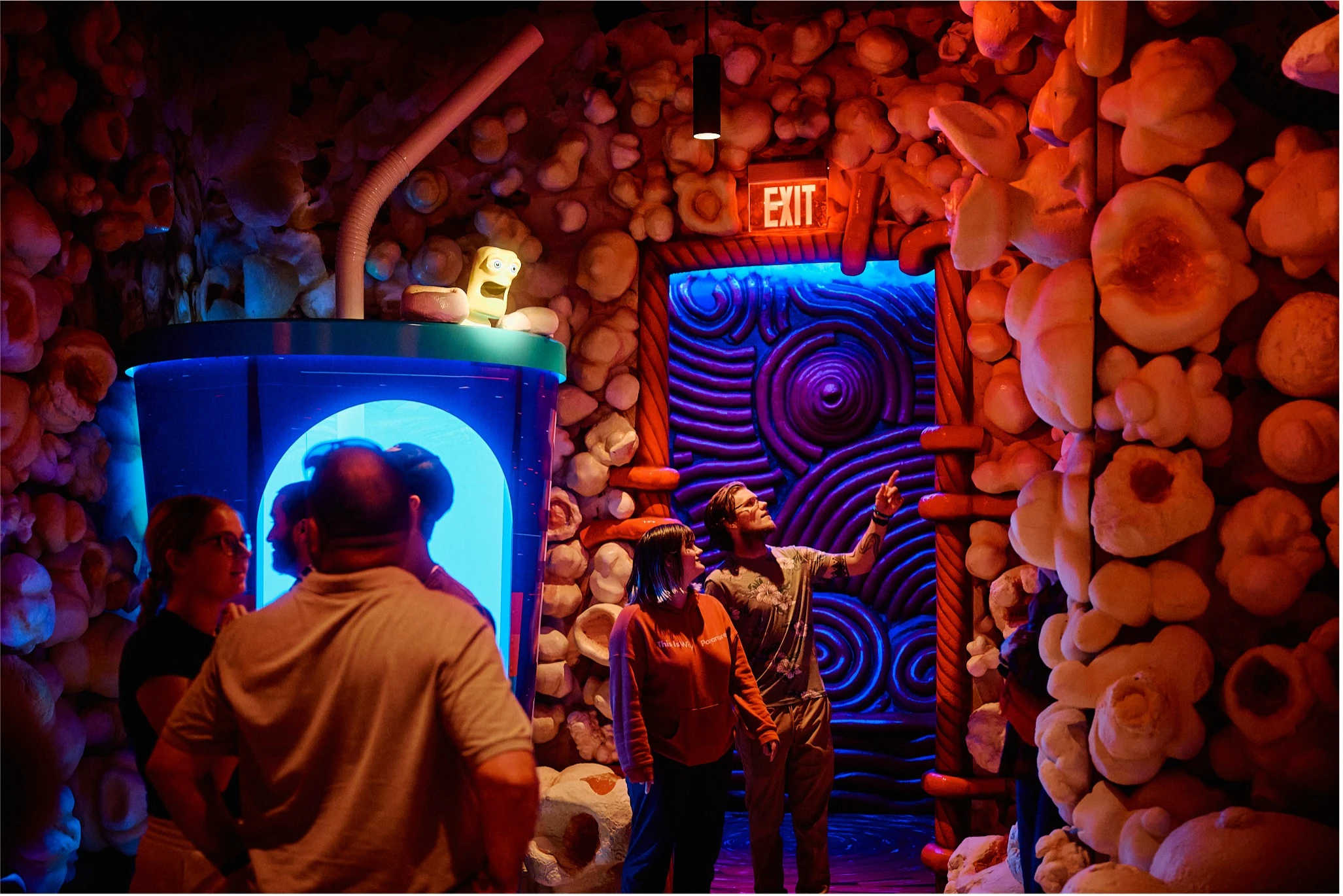 Visitors explore a surreal, brightly lit concession room at Atlas 9, surrounded by sculptural wall textures and glowing blue and red lights.