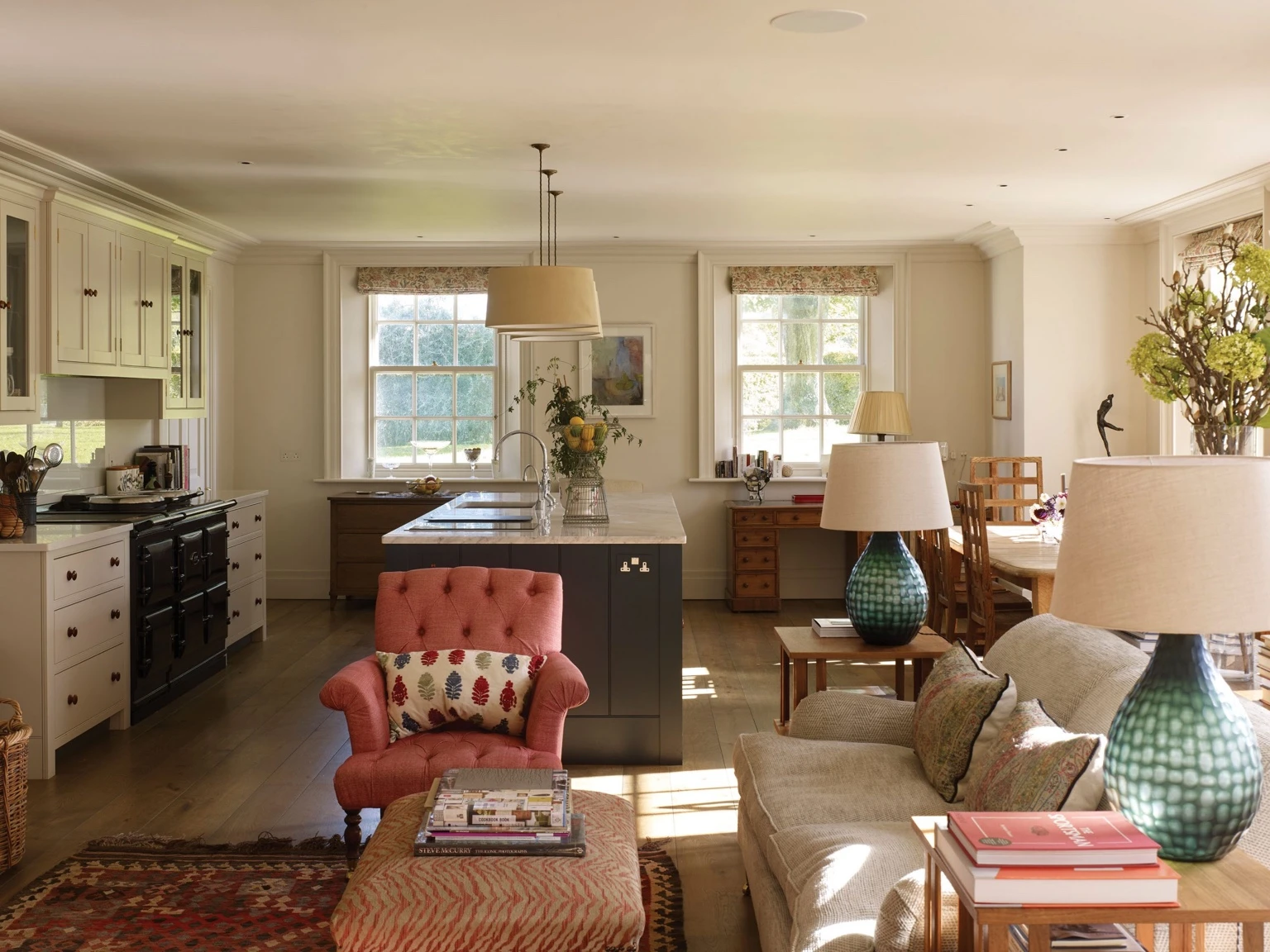 Light-filled open-plan Grade IIlisted Oxfordshire interior with a classic kitchen, dining area, and sitting room featuring warm wood floors, soft neutral furniture, and colorful accents.