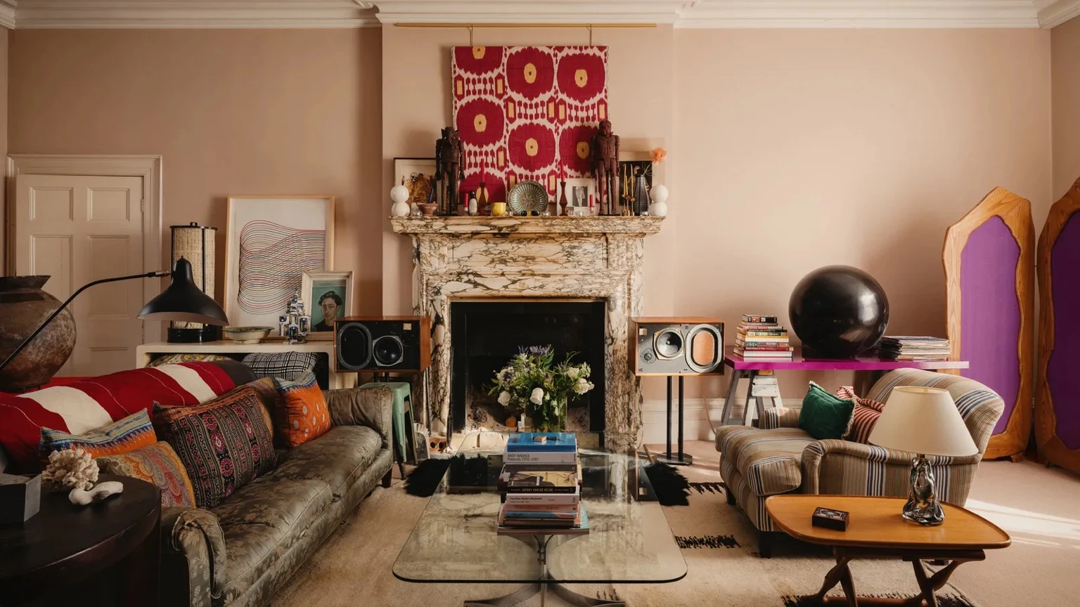 Eclectic Maida Vale living room with a marble fireplace, patterned sofas, colourful cushions, vintage speakers, books, and bold decorative objects.