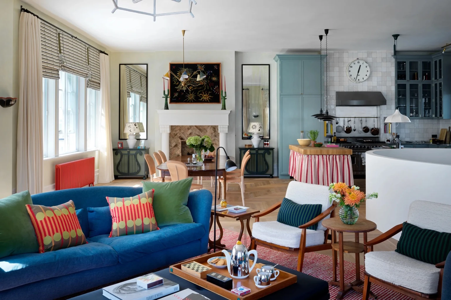 Vibrant open-plan living, dining and kitchen space with a blue sofa, patterned cushions, colourful cabinetry, and playful decor by Beata Heuman.