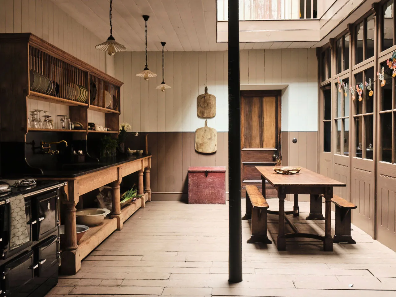 Historic kitchen at Berdoulat with open wooden shelving, long farmhouse table and benches, and paneled walls in warm brown and cream tones.