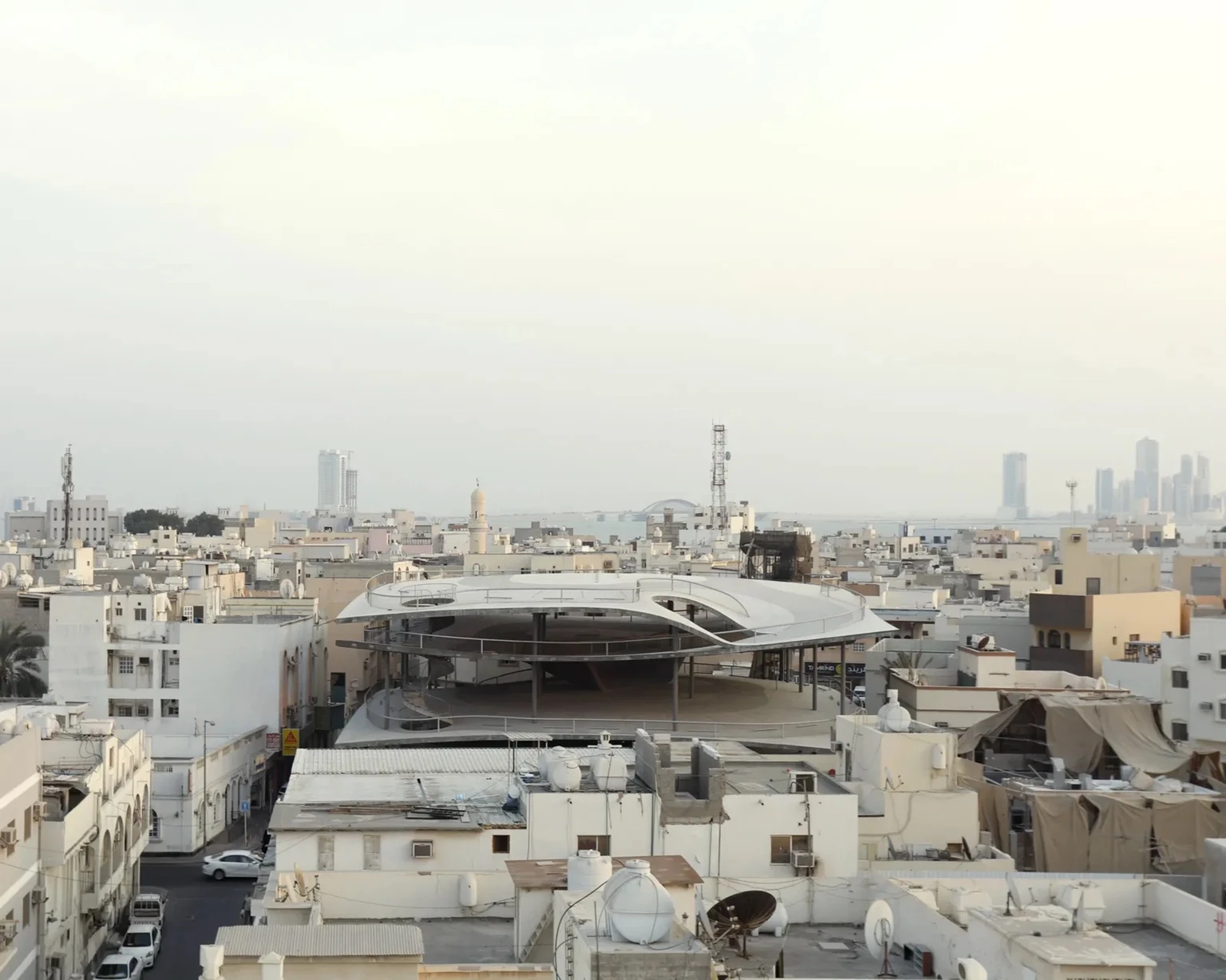 Aerial view of the shaded Car Park structure in Muharraq, Bahrain, designed by Christian Kerez, surrounded by dense low-rise buildings with the modern skyline visible in the distant haze.
