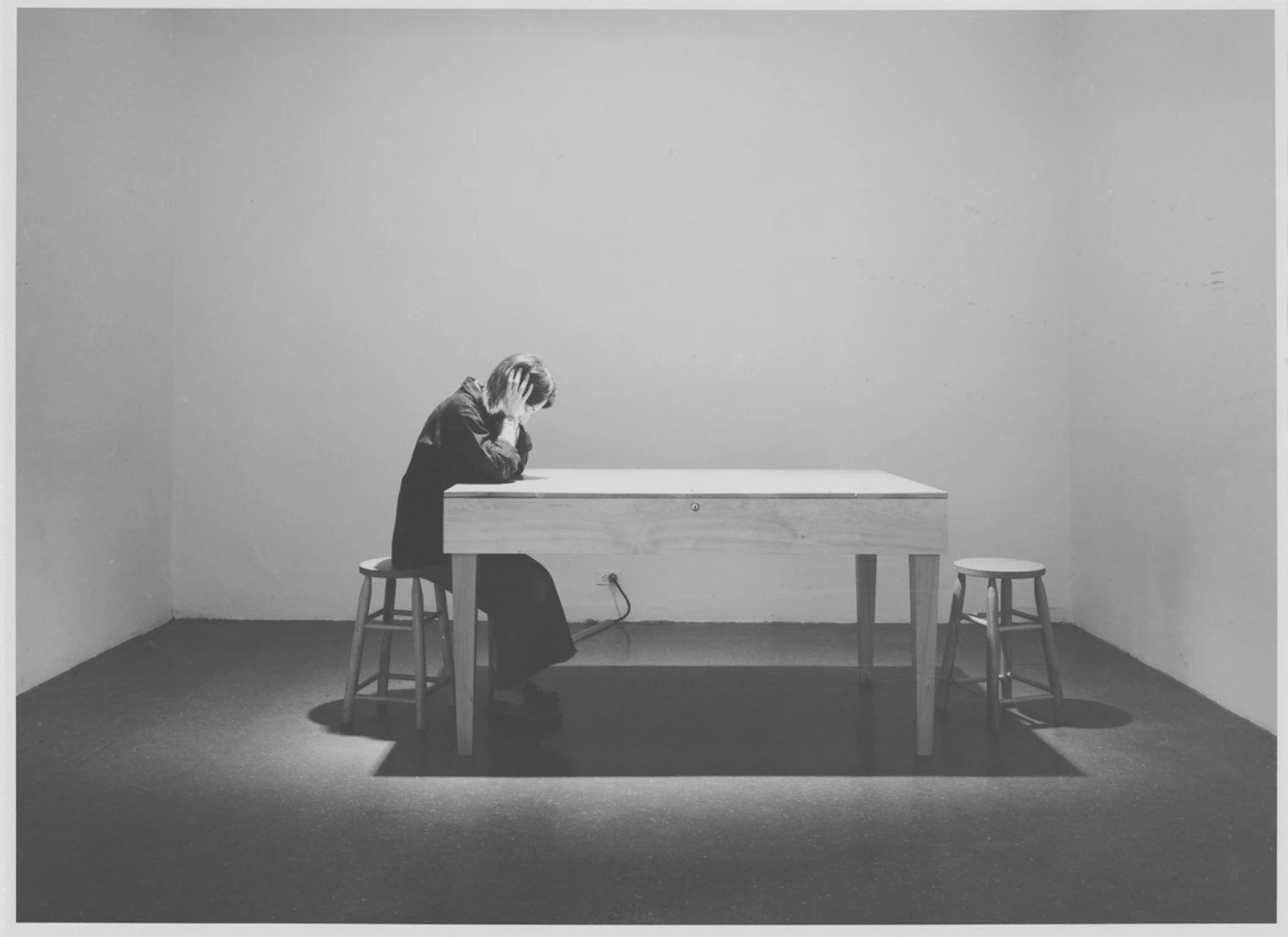 Black-and-white installation view of Laurie Anderson’s Handphone Table, showing a seated participant leaning over a table with hands covering ears, activating sound through bone conduction.
