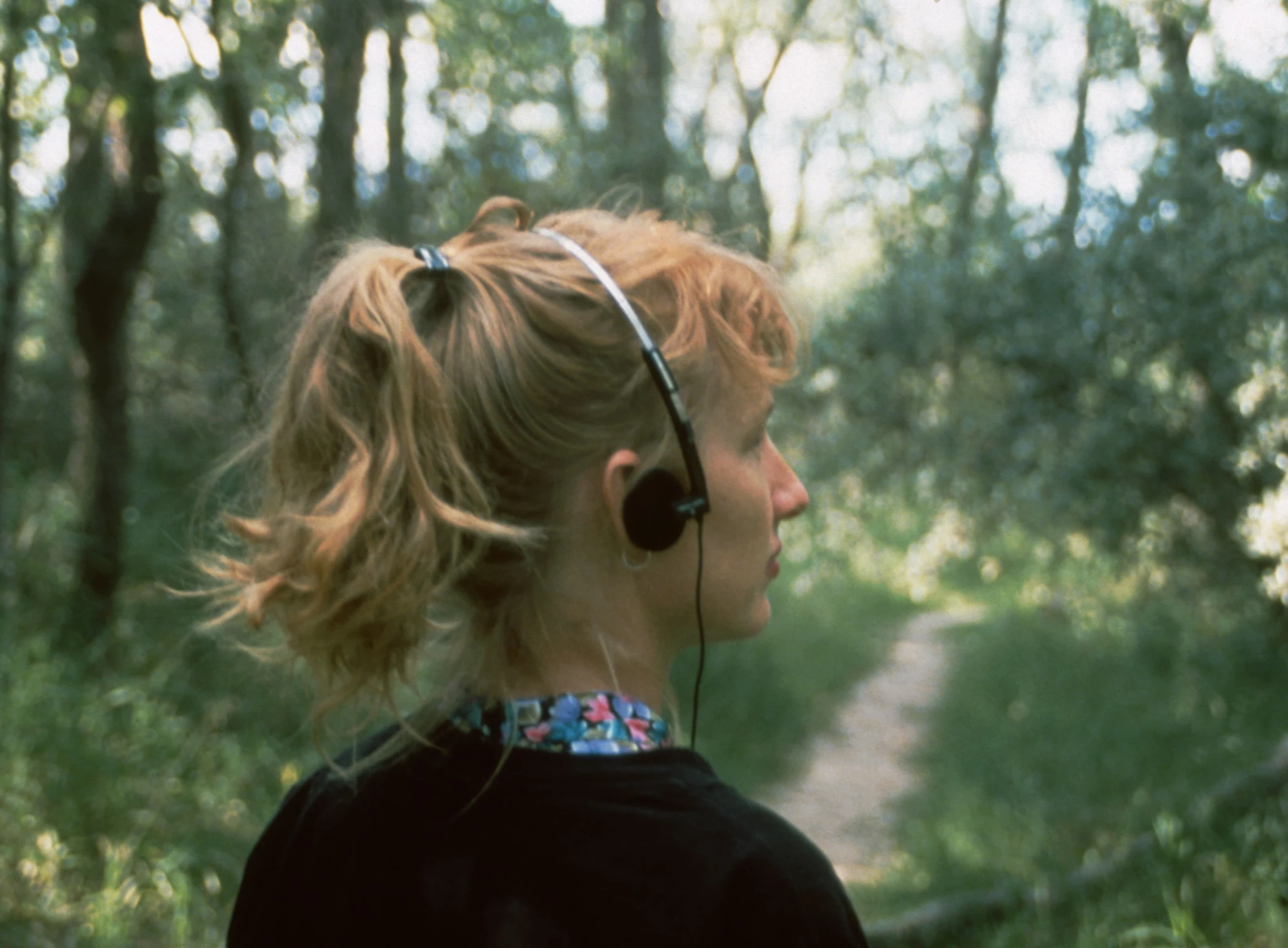Participant wearing headphones walking along a narrow forest path, listening to Janet Cardiff’s audio work Forest Walk, which guides movement through sound and narrative.