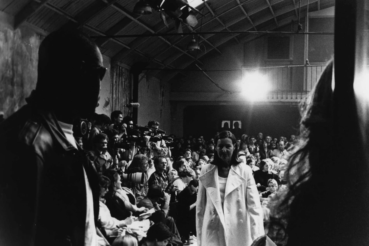 Black and white photograph of a Helmut Lang Sance de Travail runway show during the Hommes Femmes collection Winter 1993–94, showing a model walking through a seated audience