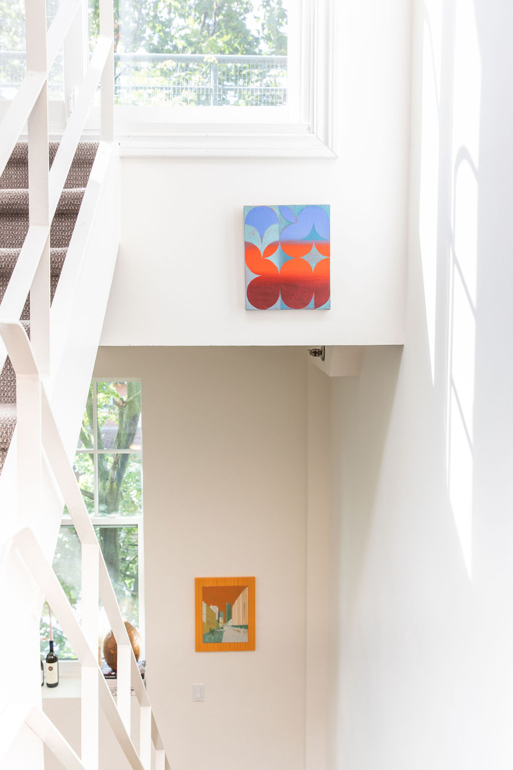 Abstract geometric red blue painting hung in modern white stairwell with second cityscape artwork below