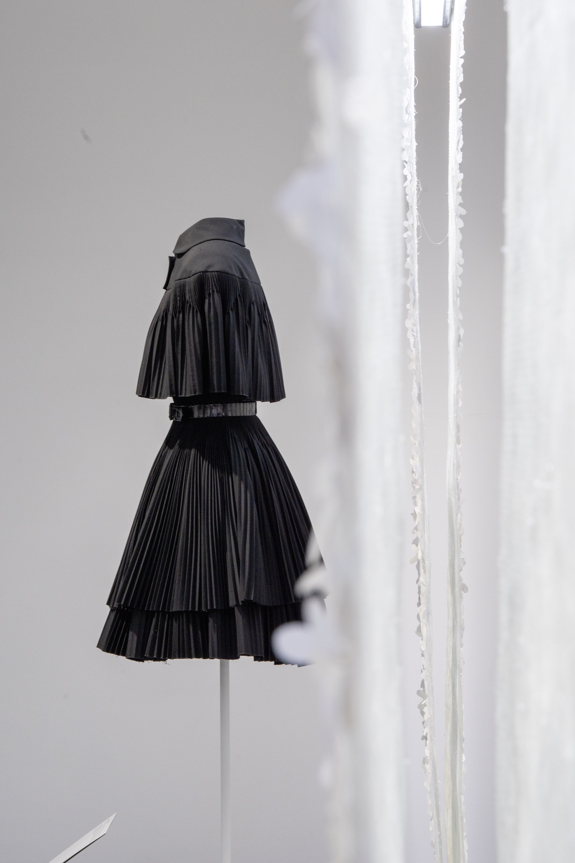 Black pleated haute couture dress with capelet on display stand, fashion exhibition
