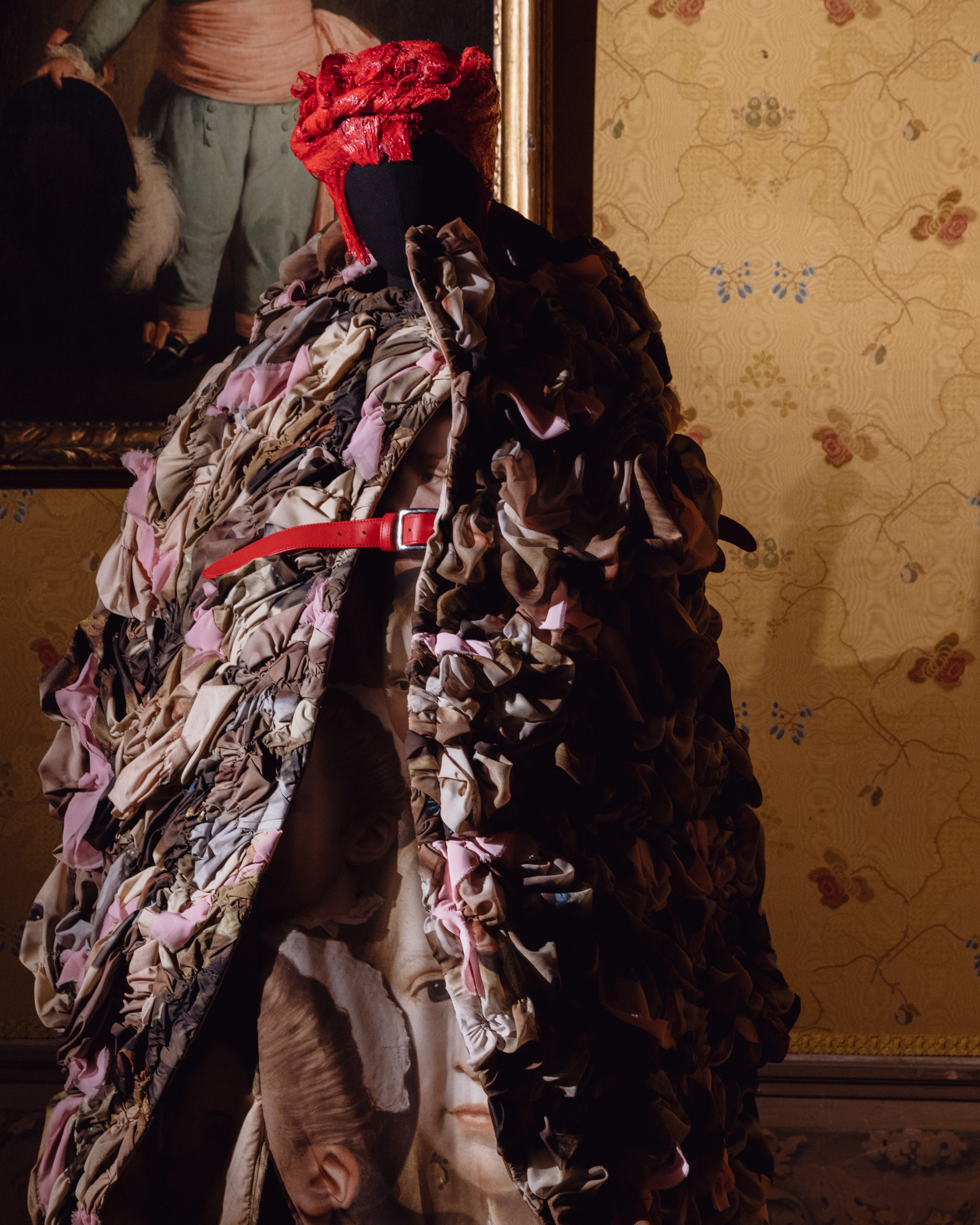 Mannequin wearing ruffled patchwork coat with red belt and sculptural red headpiece, Dries Van Noten Foundation exhibition