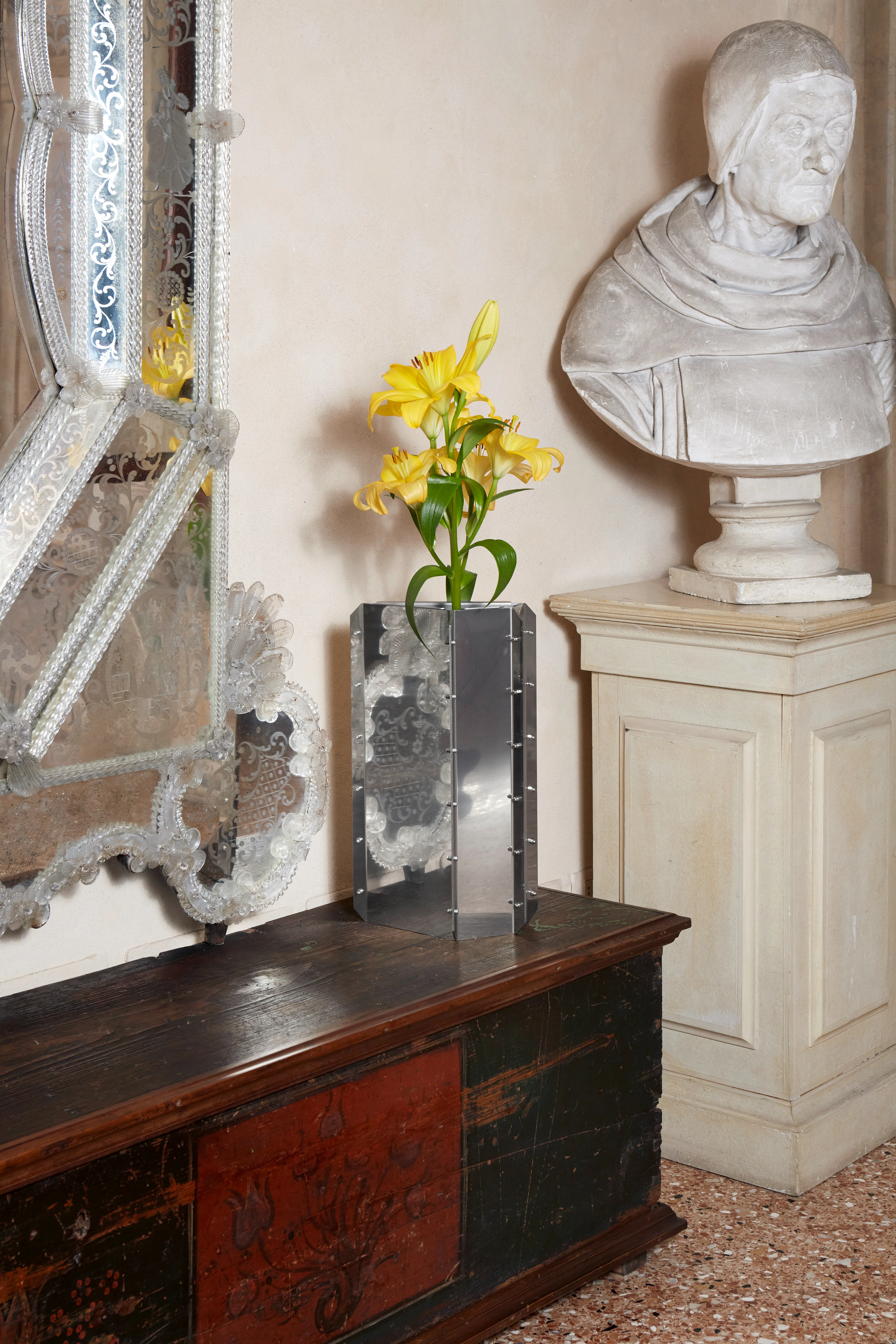 Venetian interior with marble bust, ornate Murano mirror, and modern metal vase with yellow lilies