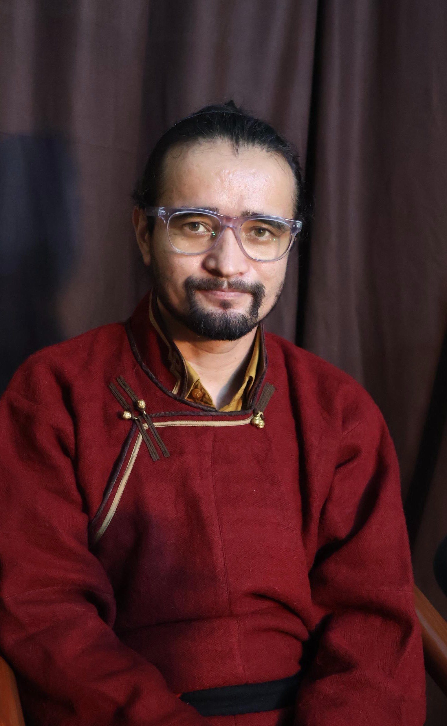 Skarma Sonam Tashi wearing red traditional Ladakhi chuba robe with clear-framed glasses